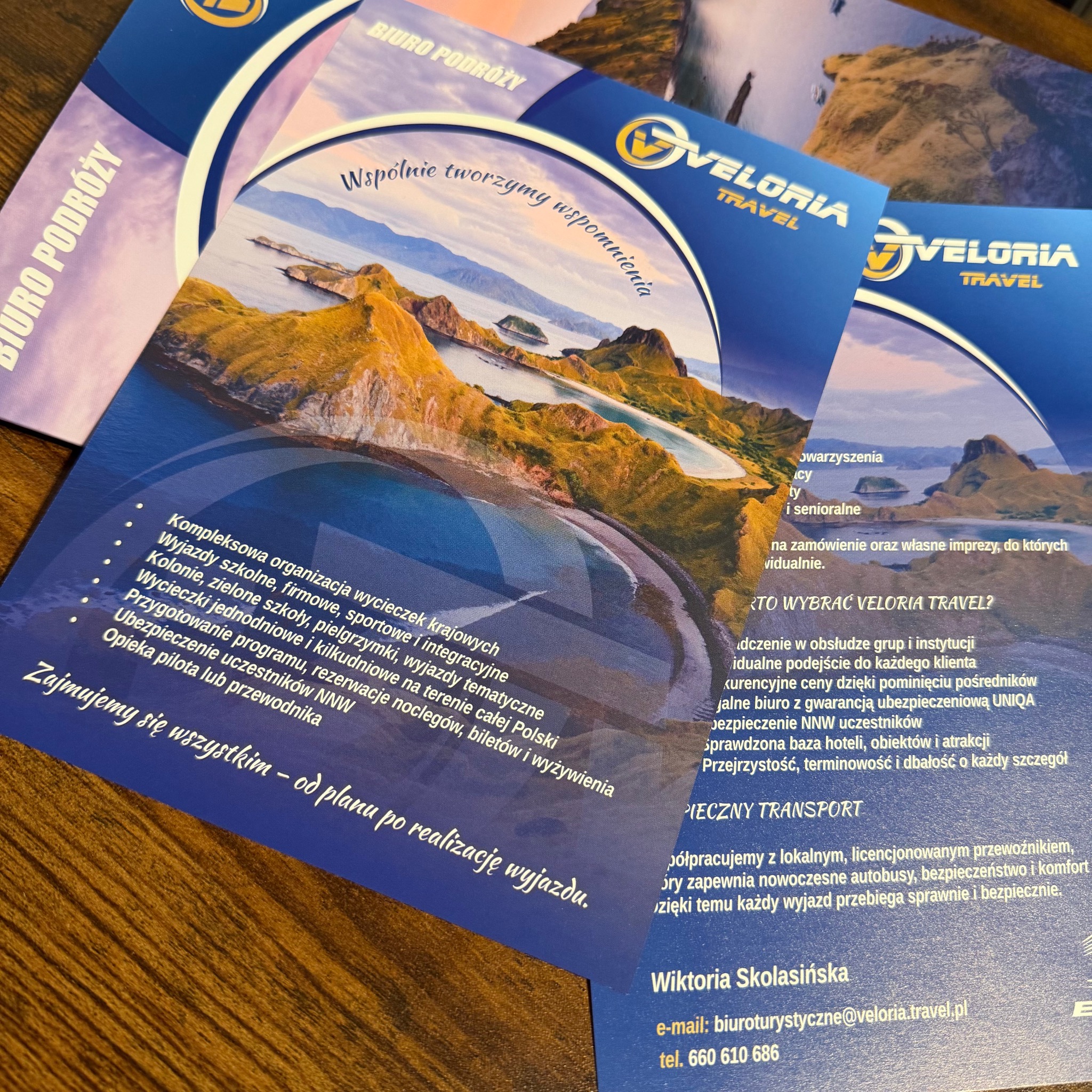 Ułożone ulotki biura podróży Veloria Travel z widokiem na malowniczy krajobraz i ofertą wycieczek krajowych, kolonii, wyjazdów firmowych i kompleksowej organizacji.