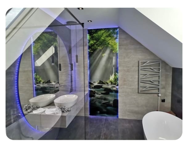 Nowoczesna łazienka na poddaszu z owalnym lustrem LED, dwoma umywalkami i grzejnikiem dekoracyjnym. Na ścianie fototapeta z motywem leśnego strumienia.