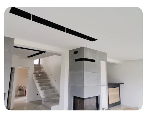 Wnętrze w trakcie wykańczania: sufit z czarnymi elementami, surowe schody betonowe, obudowa kominka z szarych płyt. Widoczne przygotowania do dalszych prac.