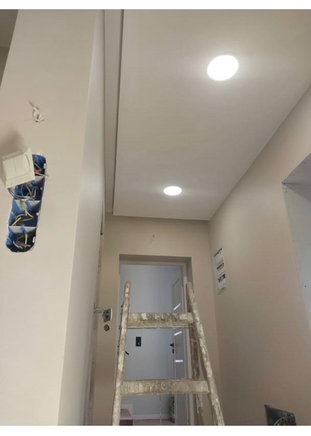 Wykończony sufit podwieszany z dwoma punktami świetlnymi. Ściany pomalowane na jasny kolor. Widoczna drabina malarska i puszka elektryczna w trakcie montażu.