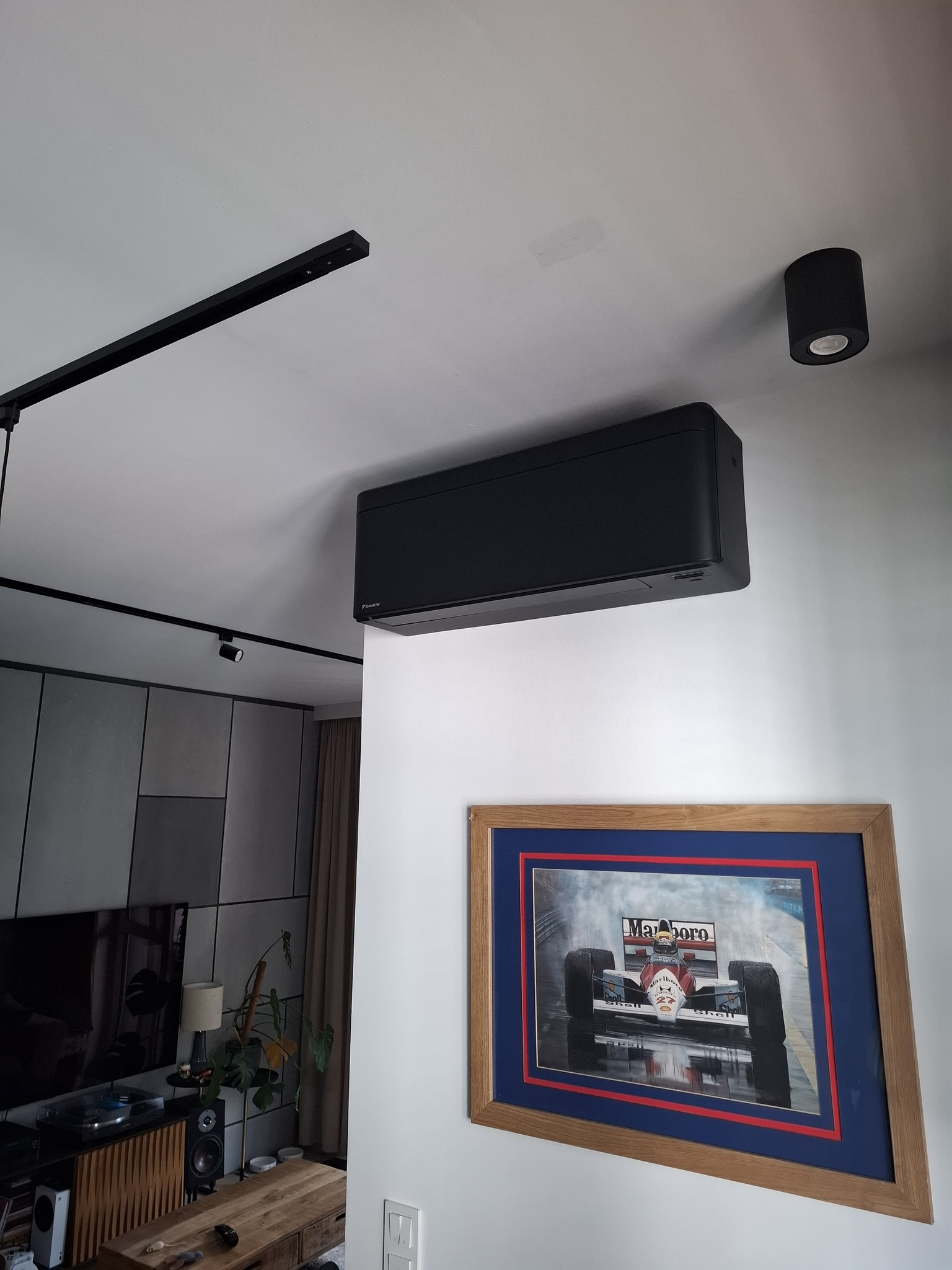Czarny klimatyzator Daikin na ścianie w nowoczesnym salonie z oświetleniem szynowym i obrazem z bolidem F1. Minimalistyczny design, eleganckie wykończenie.