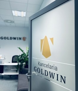 Otwarta szklana ściana z logo i napisem 'Kancelaria GOLDWIN' w nowoczesnym biurze. Widoczny fragment recepcji i logo firmy na ścianie w tle.