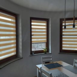 Vision House Jakub Stosio - Beżowe rolety dzień noc w drewnianych oknach, widoczne zza stołu w jadalni w Stoczku Łukowskim. Dekoracyjne osłony okienne z poziomymi pasami.