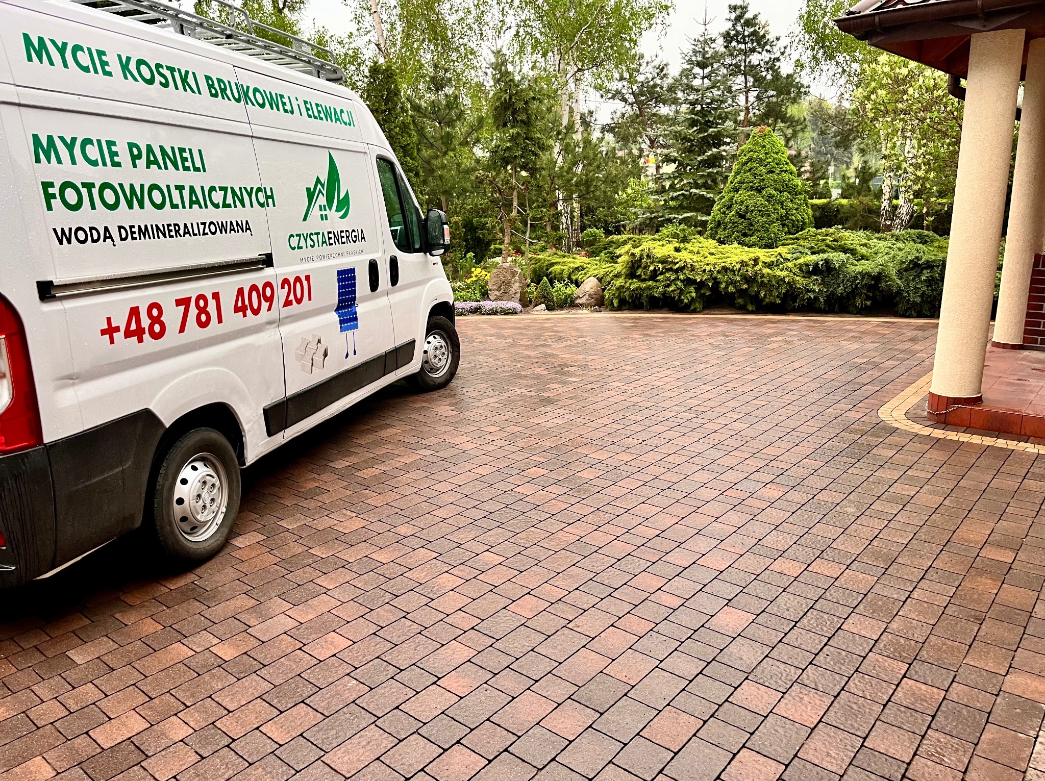 Czysta kostka brukowa po umyciu, z widocznym autem firmy oferującej mycie paneli fotowoltaicznych, kostki i elewacji. Ujęcie z niskiej perspektywy.