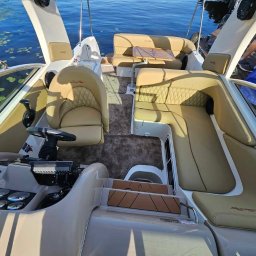 MR ATELIER SPÓŁKA Z OGRANICZONĄ ODPOWIEDZIALNOŚCIĄ - Beżowe, pikowane obicia i siedzenia w luksusowej motorówce Sea Ray, widok z kokpitu na część wypoczynkową z drewnianym stolikiem. W tle woda i roślinność.