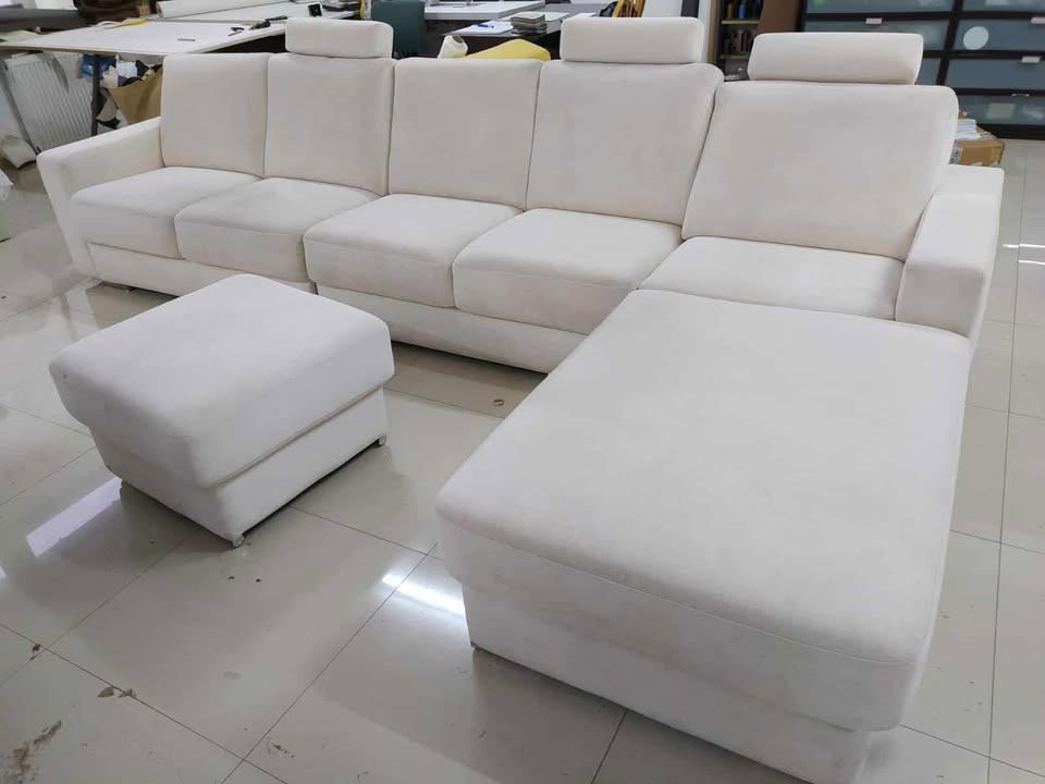 Jasny, modułowy narożnik z pufami w minimalistycznym stylu. Widoczne regulowane zagłówki i subtelne nóżki. Ujęcie z lekkiego ukosa, podkreślające przestronność mebla.