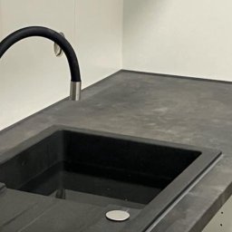 nowysilikon - Nowoczesna, czarna umywalka z elastyczną baterią na blacie z szarego kamienia, minimalistyczne wnętrze łazienki z białymi ścianami.