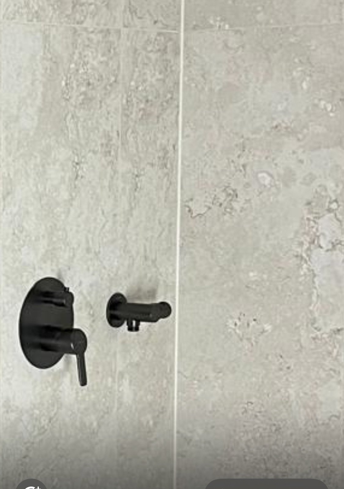 Szara ściana z płytek imitujących kamień z zamontowaną czarną, minimalistyczną baterią prysznicową. Nowoczesne wykończenie łazienki.