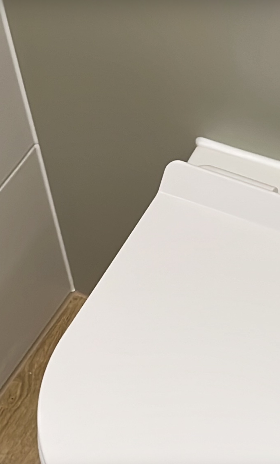 Nowoczesna toaleta z deską wolnoopadającą, minimalistyczny design, jasne kolory, drewnopodobna podłoga, szara ściana. Detal wykończenia łazienki.