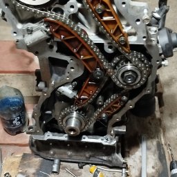 Zarasprint LTD - Rozłożony silnik samochodowy z łańcuchem rozrządu i narzędziami na drewnianym podłożu w warsztacie w Przasnyszu. Widoczne detale mechaniczne i elementy silnika.