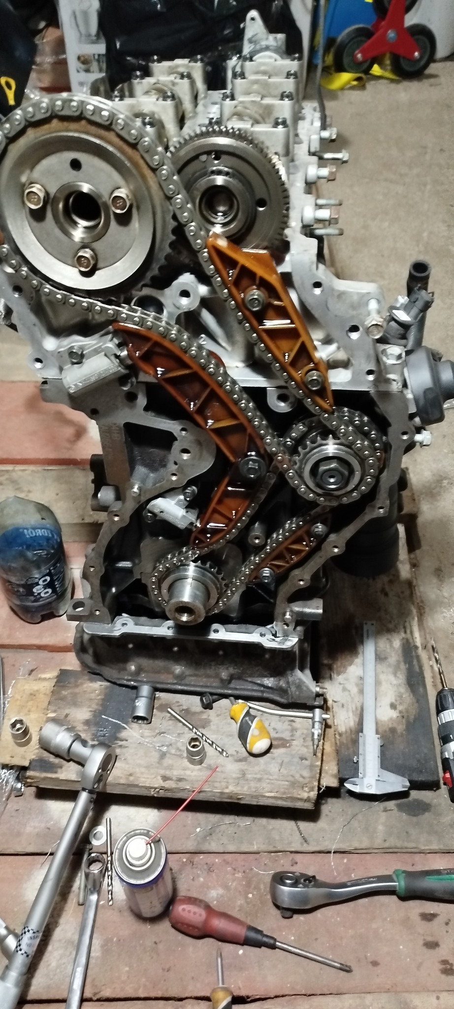 Rozłożony silnik samochodowy z łańcuchem rozrządu i narzędziami na drewnianym podłożu w warsztacie w Przasnyszu. Widoczne detale mechaniczne i elementy silnika.