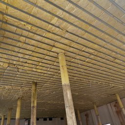 MM-Invest - z pasją i pod klucz - Sufit podwieszany z izolacją z wełny mineralnej, widok z dołu, metalowa konstrukcja, podpory tymczasowe, surowy stan wykończenia, okno z lewej strony.