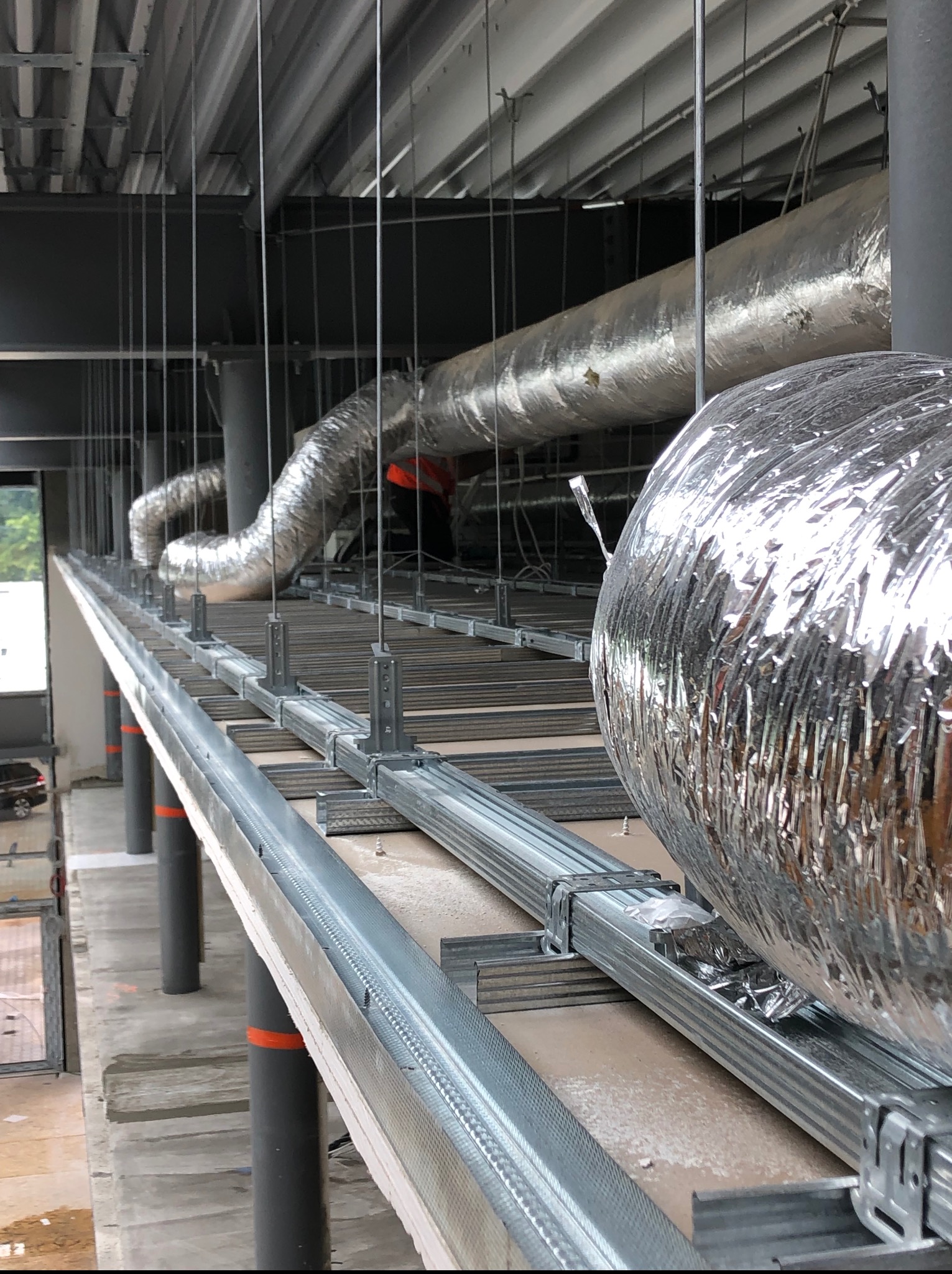 Metalowa konstrukcja sufitu podwieszanego z widocznymi elementami wentylacji, w trakcie montażu w surowym wnętrzu budynku.