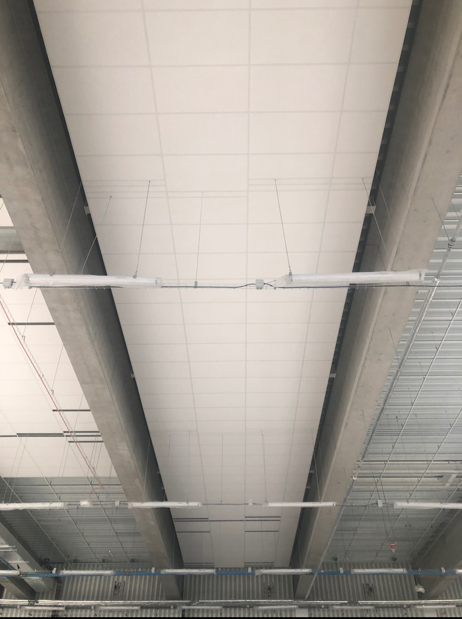 Sufit podwieszany kasetonowy z widocznymi elementami konstrukcyjnymi i oświetleniem w folii ochronnej, w trakcie montażu w przestrzeni biurowej.