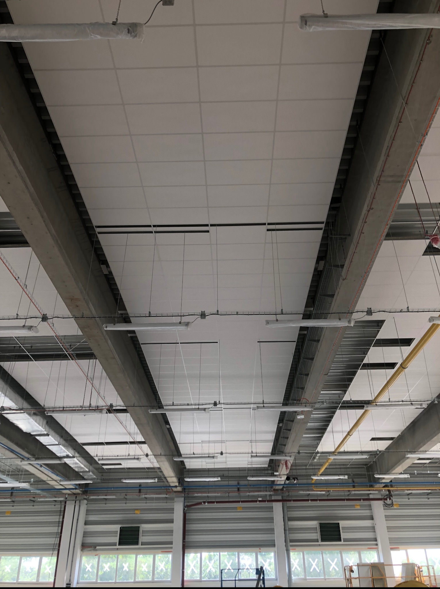 Sufit podwieszany z płyt kartonowo-gipsowych w hali przemysłowej, widok z dołu, widoczne elementy konstrukcyjne i instalacje.