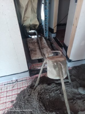 Przygotowanie mieszanki na ogrzewanie podłogowe. Widoczna instalacja grzewcza, mieszadło i surowa masa. Prace wykończeniowe wewnątrz budynku.