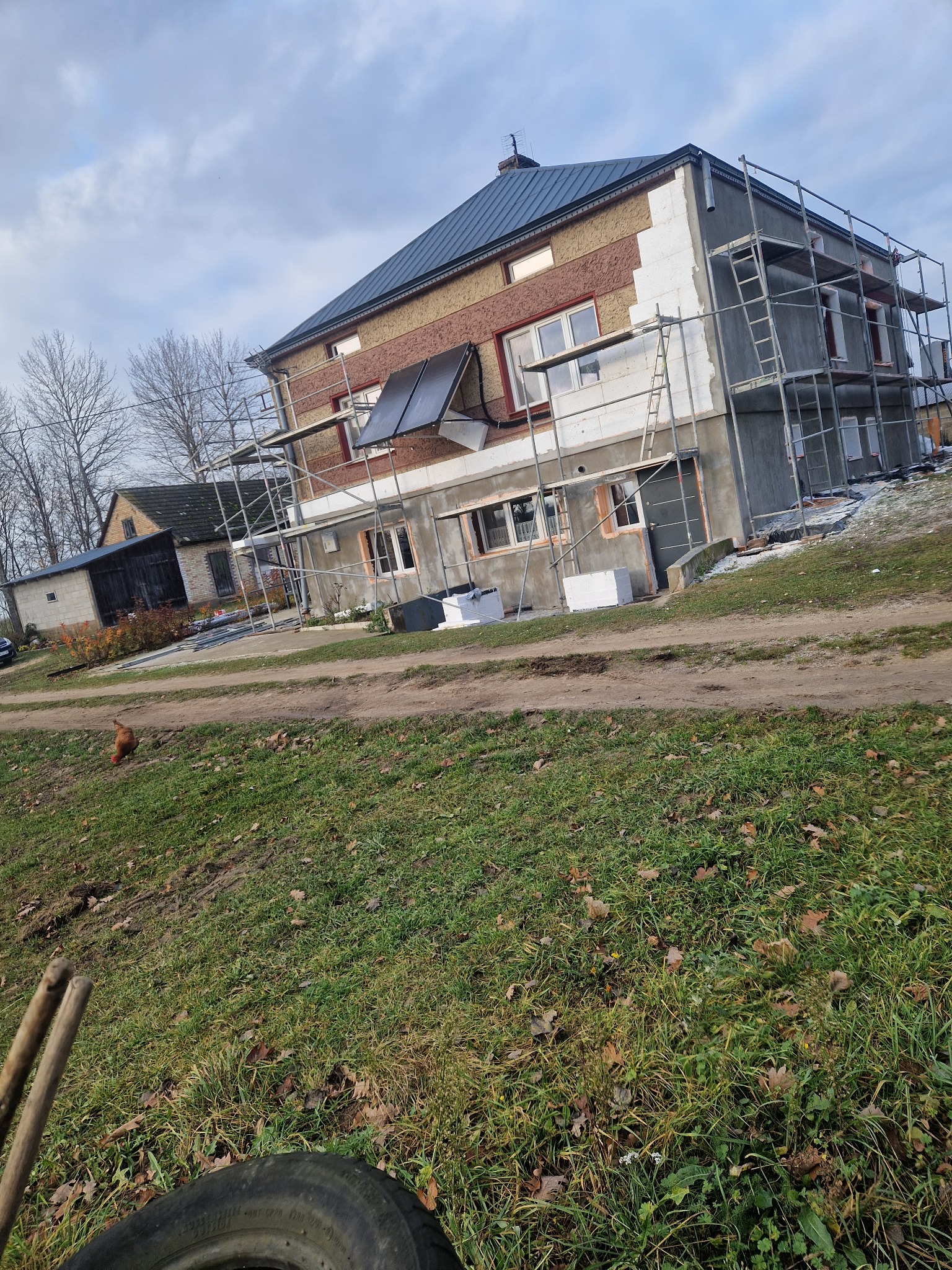 Dom w trakcie ocieplania, widoczne rusztowania i częściowo ocieplona ściana styropianem. Na dachu panele słoneczne. Ujęcie z dołu, lekko pod kątem.