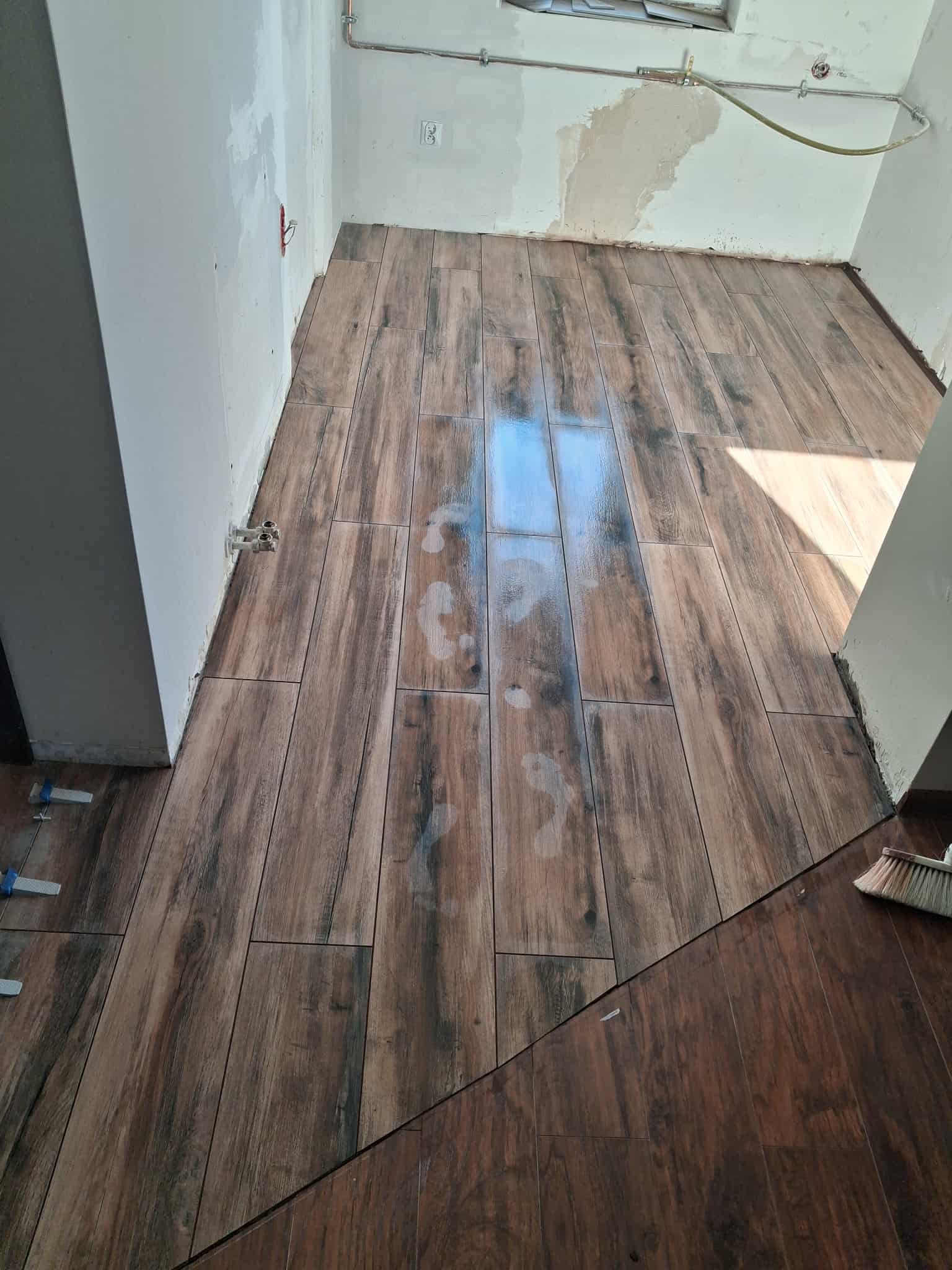 Ułożona podłoga z płytek imitujących drewno w trakcie remontu łazienki. Widoczne ślady stóp, białe ściany w trakcie wykończenia i narzędzia glazurnicze.