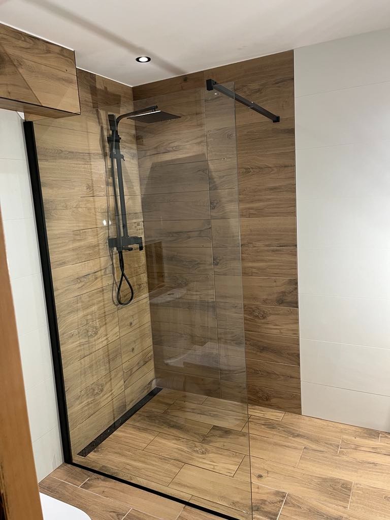Kabina prysznicowa walk-in z czarnymi profilami i deszczownicą, wykończona płytkami imitującymi drewno i białymi płytkami. Nowoczesny design łazienki.
