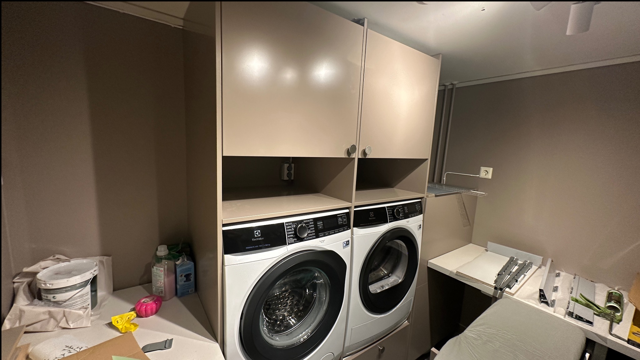 Dwie pralki Electrolux w zabudowie meblowej z szafkami, widoczne gniazdko elektryczne. Ustawienie pionowe, oszczędność miejsca w małej łazience.