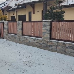 FIRMA HANDLOWA RO - Producent siatki ogrodzeniowej - Nowoczesne ogrodzenie z elementami betonowymi i drewnianymi lamelami w brązowym odcieniu, brama wejściowa, zimowy krajobraz z ośnieżonym terenem.