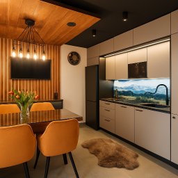 EM Nieruchomości Ewa Mozdyniewicz - Nowoczesna kuchnia z jadalnią: beżowe szafki, czarny sprzęt, drewniane akcenty i widok na góry na szklanym panelu. Pomarańczowe krzesła przy stole.