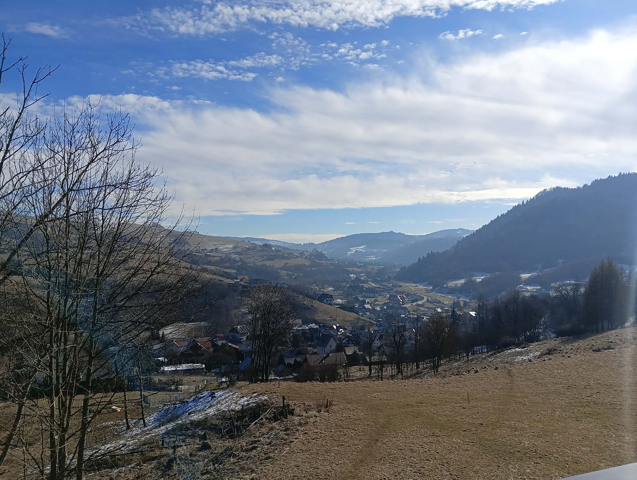 Malowniczy krajobraz górski z widokiem na osadę, błękitne niebo z chmurami i drzewa na pierwszym planie. Zimowy klimat, naturalne światło.