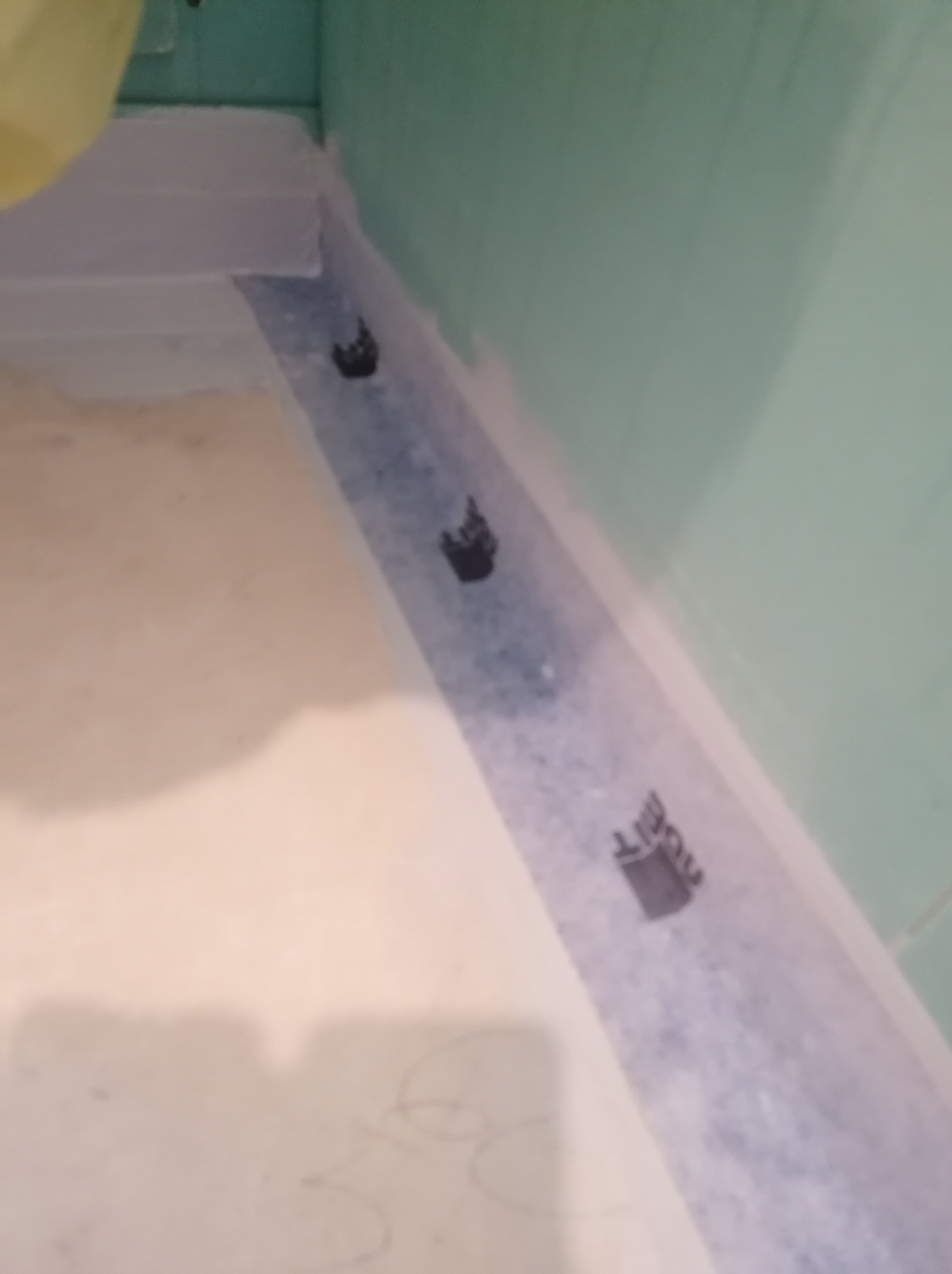 Przygotowanie podłoża pod hydroizolację w łazience. Widoczne taśmy uszczelniające i narożniki w strefie prysznicowej. Ściany zabezpieczone folią w płynie.