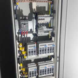 Wojciech Pietrzak Elektryk - Rozdzielnica elektryczna z zainstalowanymi bezpiecznikami, przewodami i szynami, widok z bliska na wnętrze szafy sterowniczej z elementami zabezpieczeń.