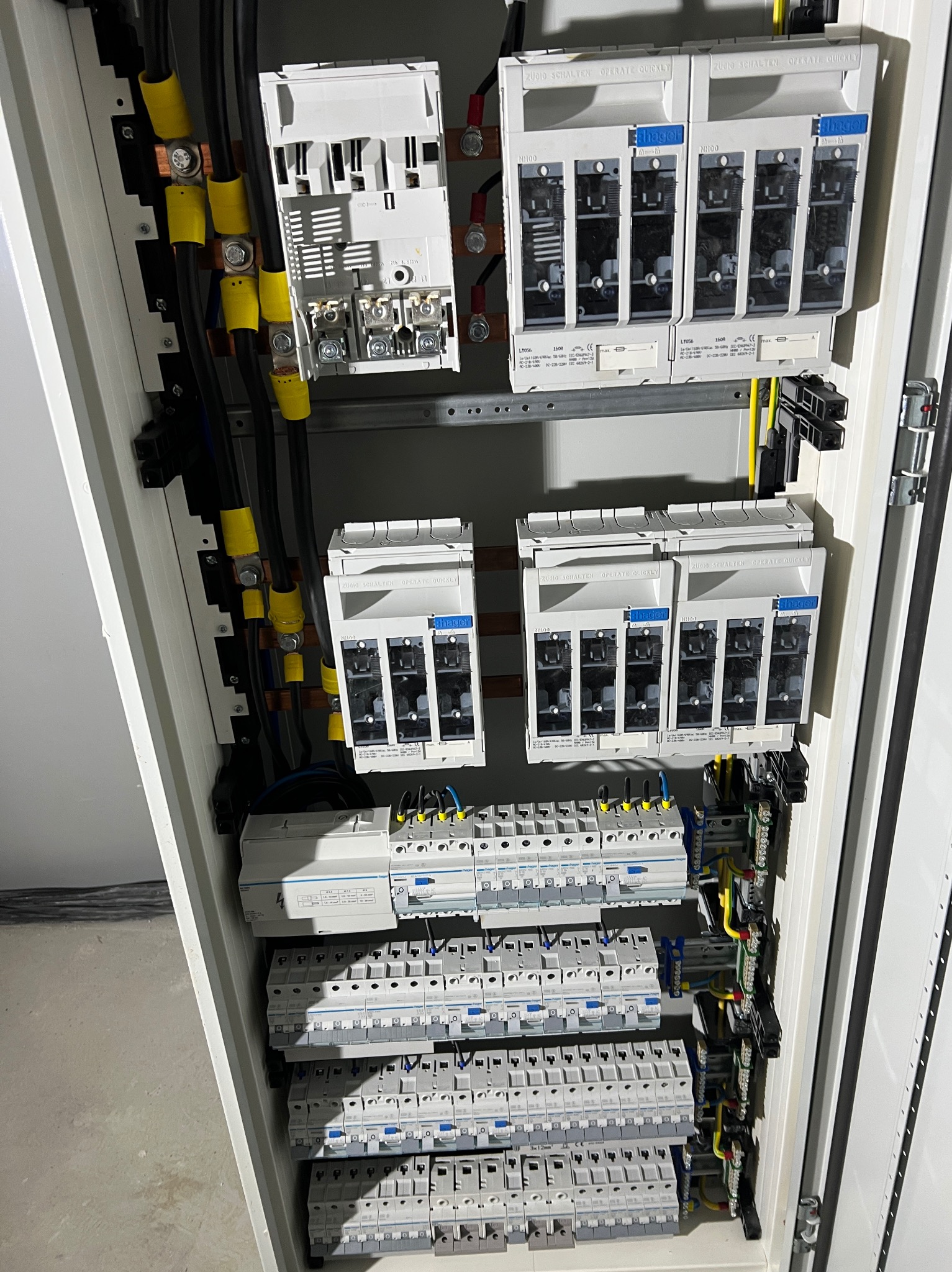 Rozdzielnica elektryczna z zainstalowanymi bezpiecznikami, przewodami w żółtych osłonach i szyną DIN. Widok z bliska na wnętrze szafy elektrycznej.