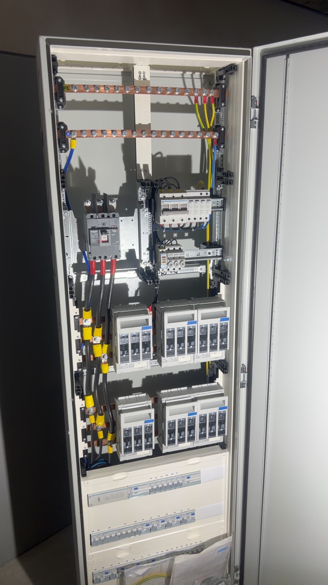 Rozdzielnica elektryczna z zainstalowanymi bezpiecznikami, przewodami i szynami, widok z bliska na wnętrze szafy sterowniczej z elementami zabezpieczeń.