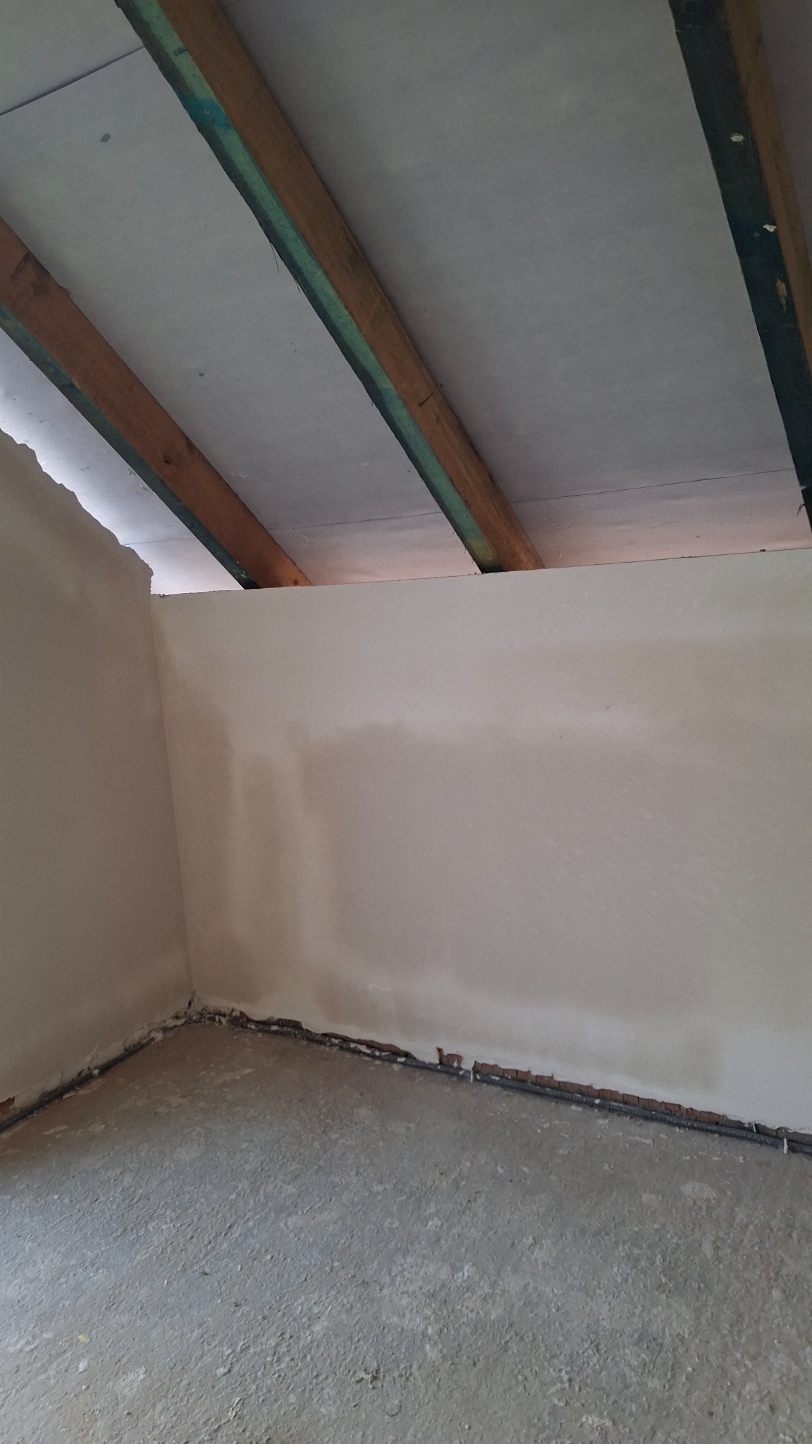 Świeżo otynkowane wnętrze poddasza z widocznymi drewnianymi belkami stropowymi i instalacją przy podłodze, gotowe do dalszych prac wykończeniowych.