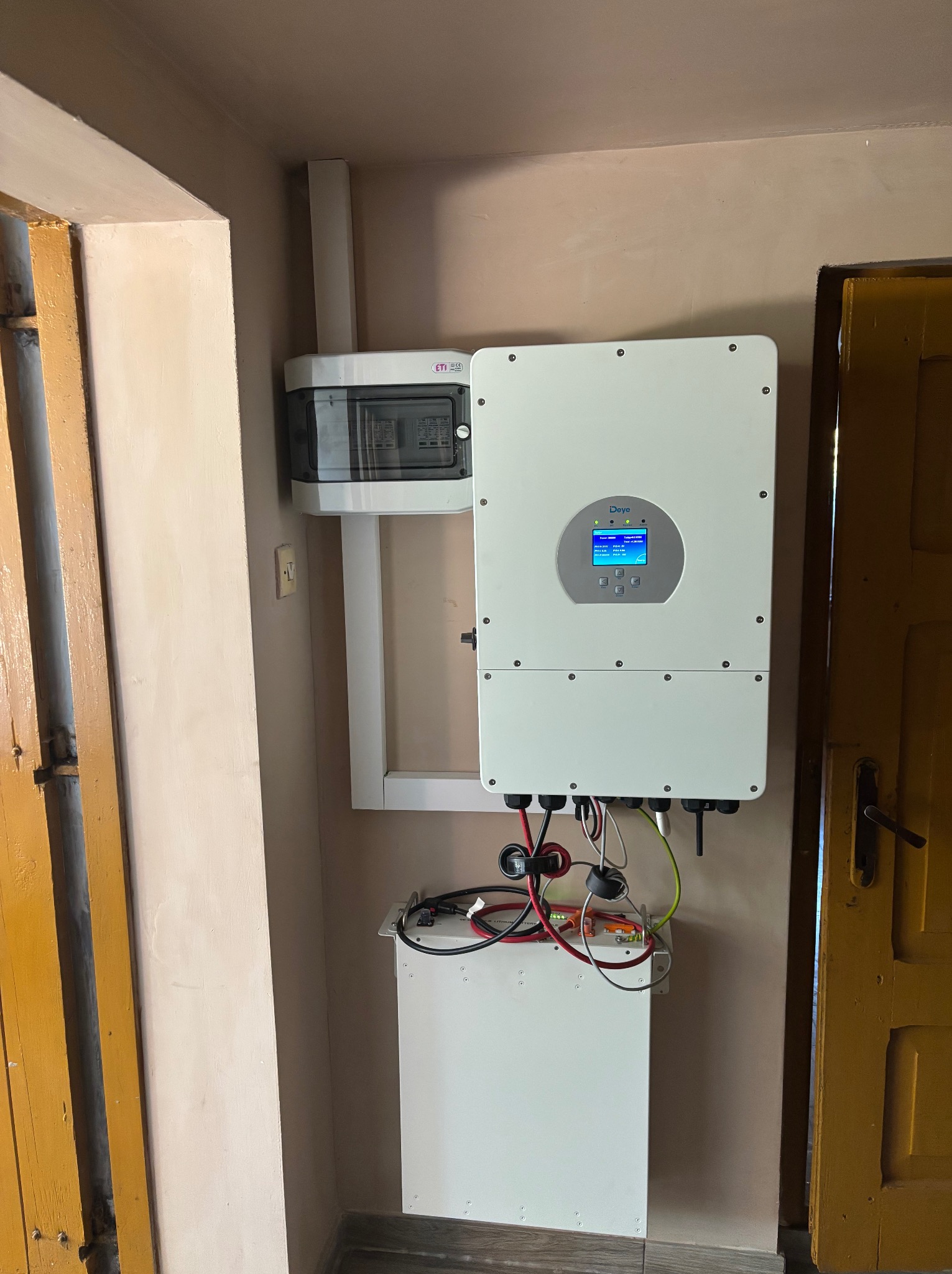 Zamontowany inwerter fotowoltaiczny marki Deye z podłączonymi kablami, obok skrzynka elektryczna. Widoczne elementy instalacji wewnątrz budynku.