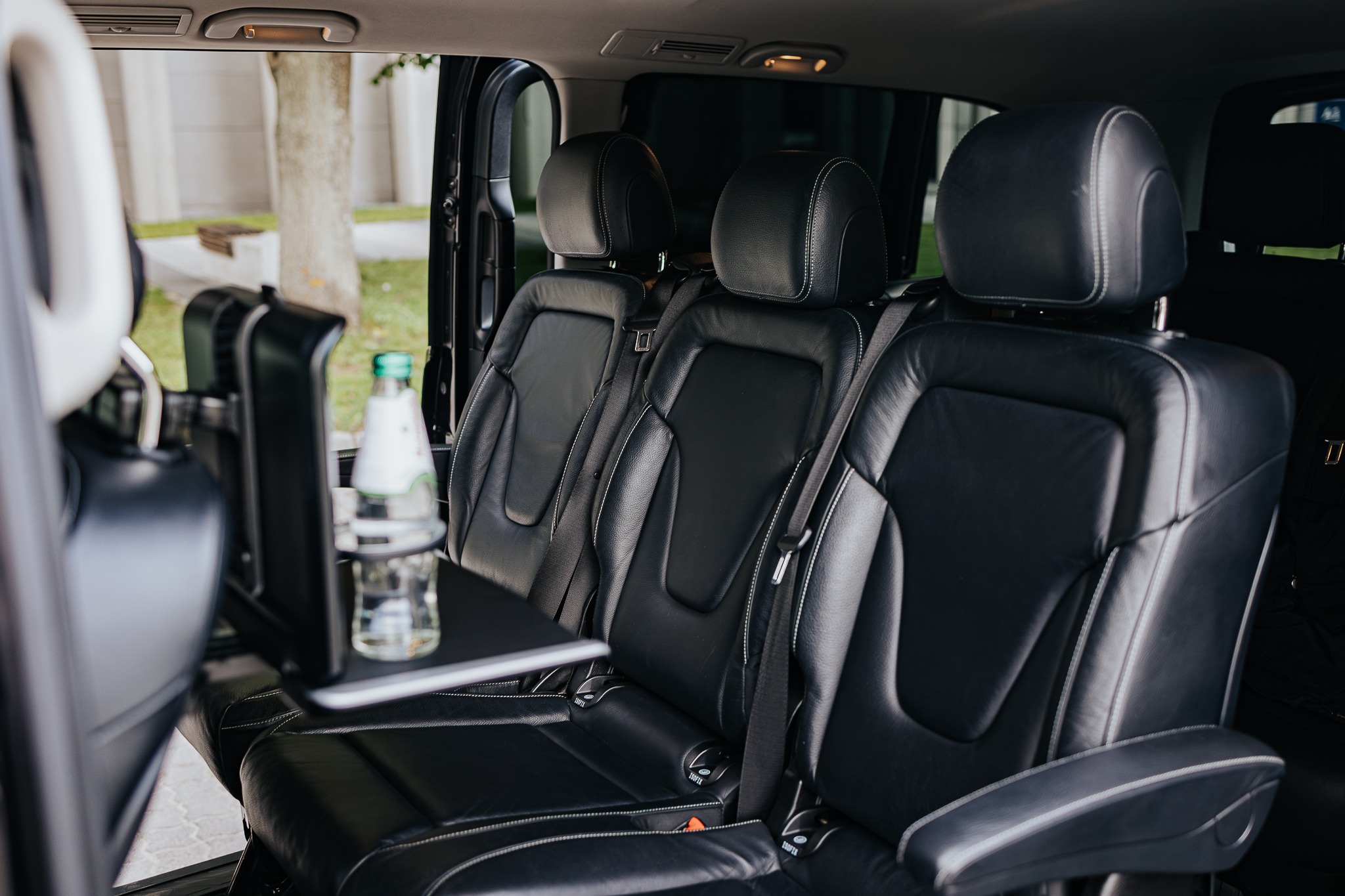 Wnętrze luksusowego busa z czarnymi skórzanymi fotelami, rozkładanym stolikiem i butelką wody. Widok na wygodne siedzenia pasażerów podczas podróży.