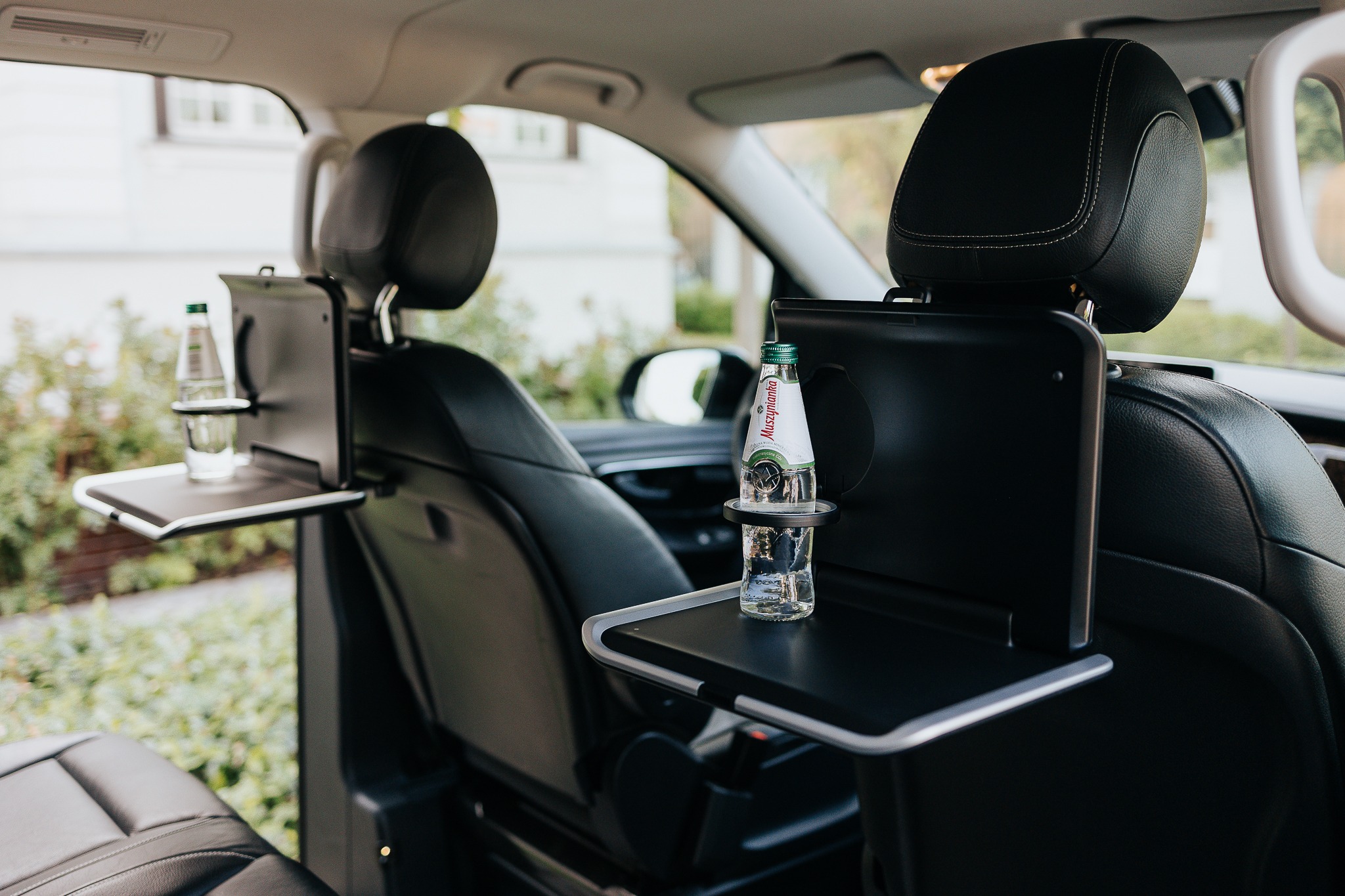 Wnętrze luksusowego busa z rozkładanymi stolikami i butelką wody mineralnej Muszynianka, zapewniające komfortową podróż pasażerom.