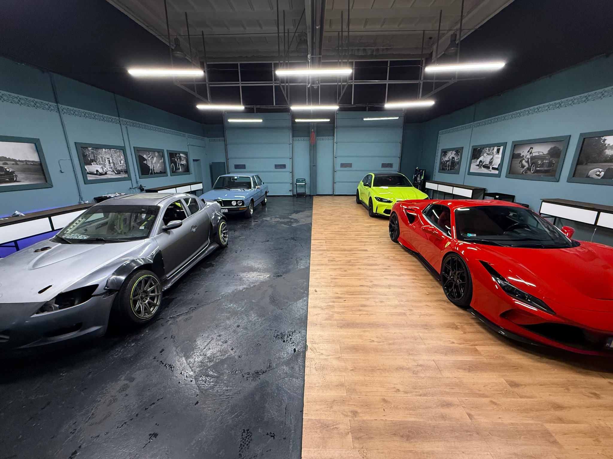 Garaż z czterema samochodami: czerwonym Ferrari, żółtym Lamborghini, niebieskim BMW i szarym Mazda RX-8. Ściany zdobią czarno-białe zdjęcia aut.