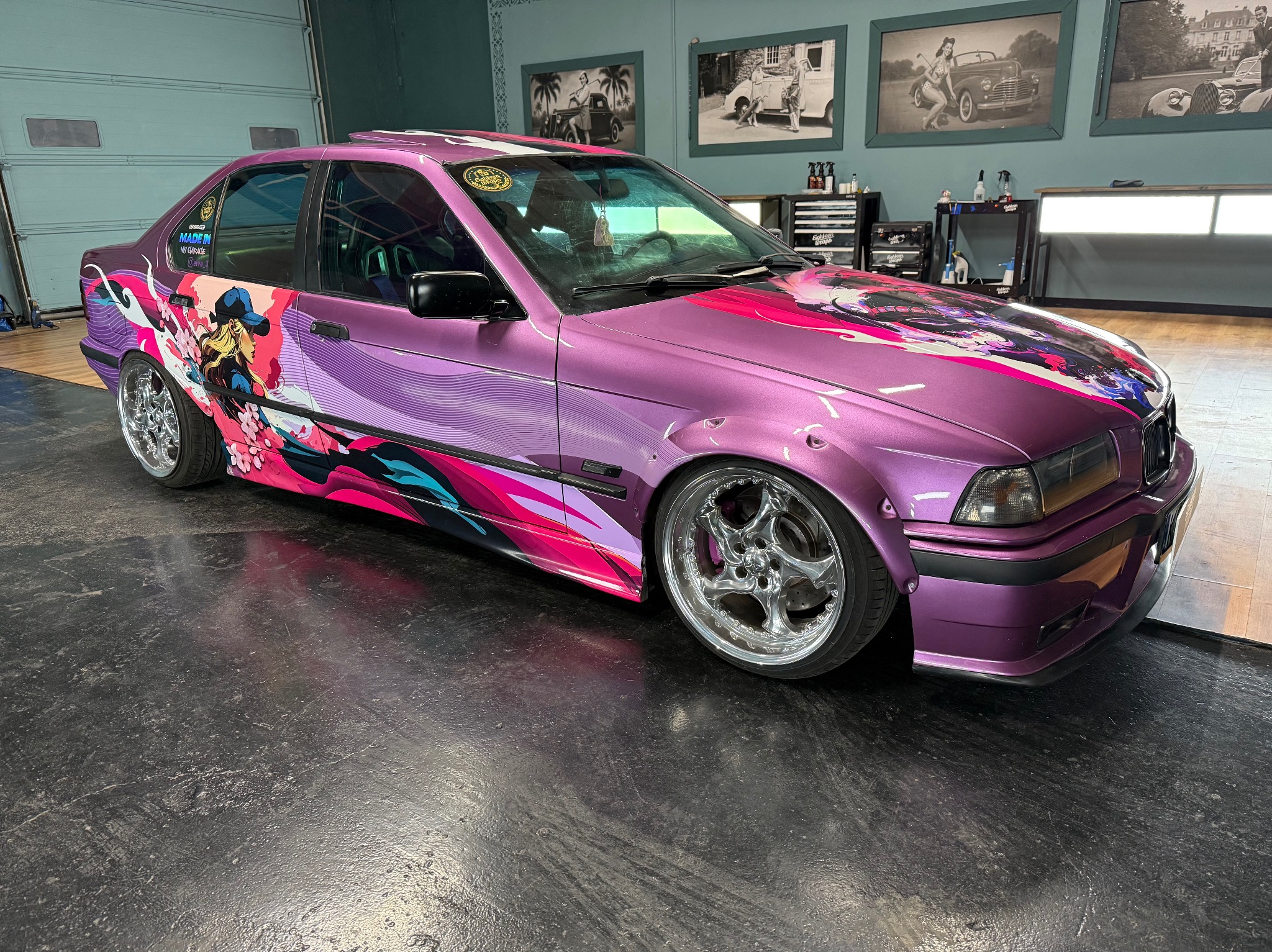 Liliowy BMW E36 po oklejeniu folią z grafiką anime, chromowane felgi, widok z boku w warsztacie. Unikalny design i kolorystyka.