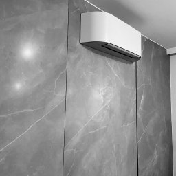 Rybski Investment - Nowoczesny klimatyzator ścienny, biały, zamontowany na szarej ścianie imitującej marmur. Minimalistyczny design, widok z dołu, oświetlenie górne.
