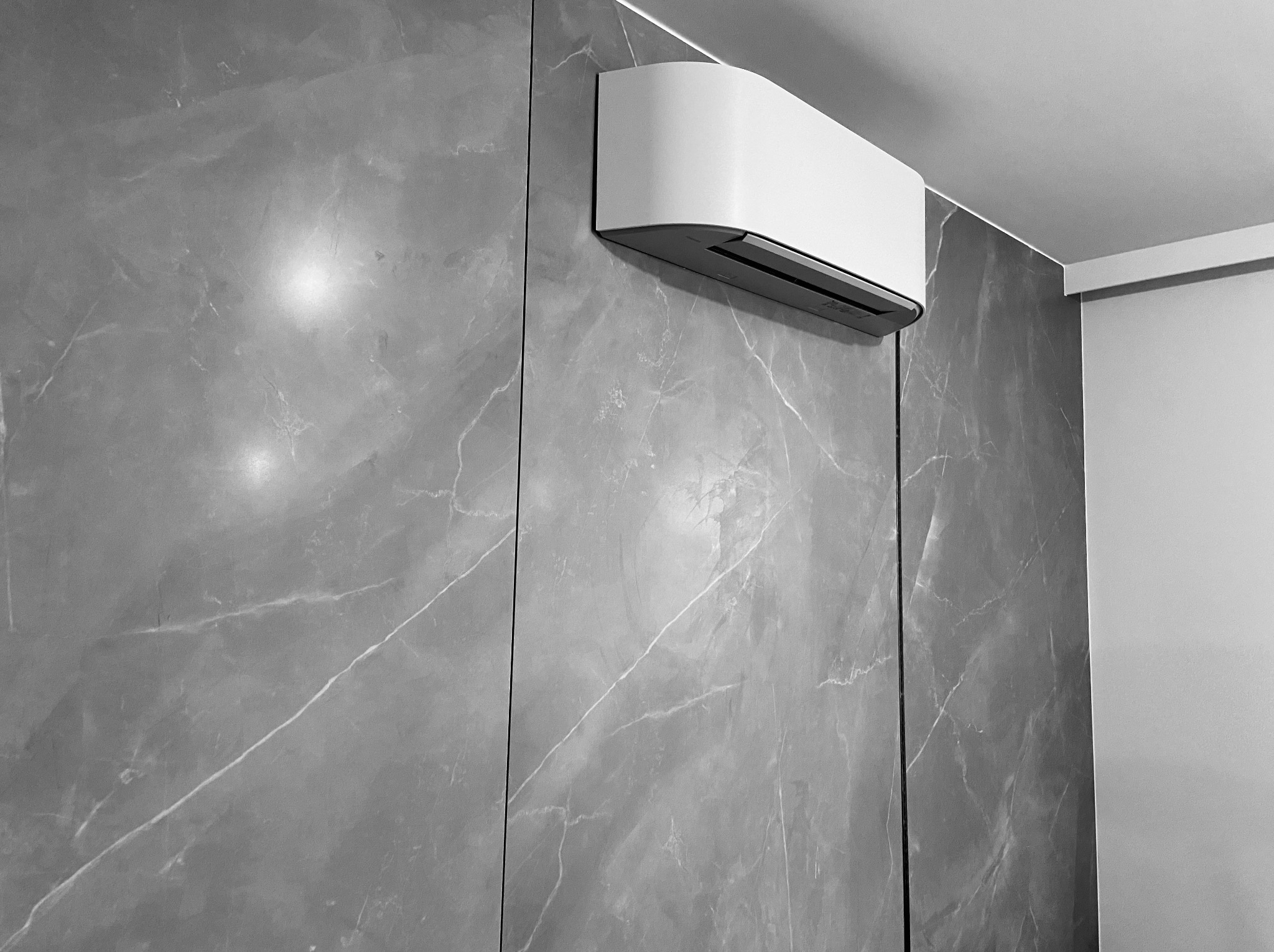 Nowoczesny klimatyzator ścienny, biały, zamontowany na szarej ścianie imitującej marmur. Minimalistyczny design, widok z dołu, oświetlenie górne.