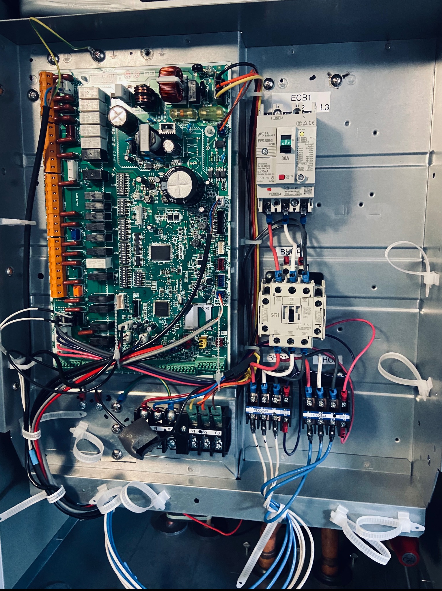 Wnętrze urządzenia z płytą sterującą, bezpiecznikiem 30A i licznymi przewodami. Widoczne złącza, kondensatory i inne komponenty elektroniczne. Praca przy instalacji elektrycznej.