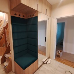 MALWA MEBLE Dariusz Jewulski - Funkcjonalna zabudowa przedpokoju z siedziskiem obitym zieloną tkaniną, wkomponowana w szafę z lustrem. Widoczne schody i fragment podłogi z butami.