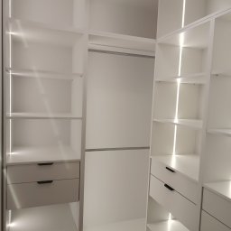 MALWA MEBLE Dariusz Jewulski - Biała, nowoczesna szafa wnękowa z oświetleniem LED, widoczne półki i szuflady z minimalistycznymi uchwytami. Jasne wnętrze garderoby.
