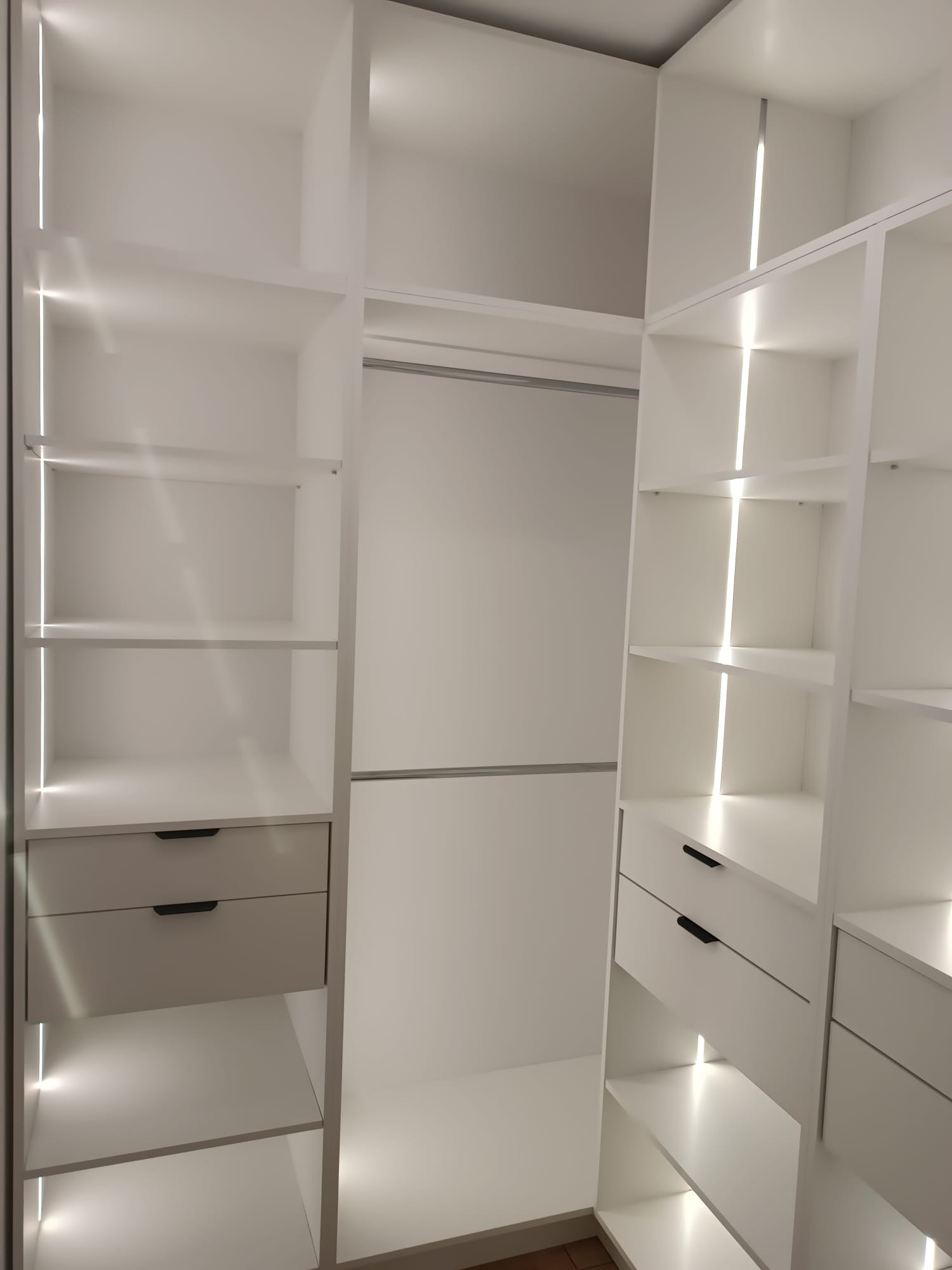 Biała, nowoczesna szafa wnękowa z oświetleniem LED, widoczne półki i szuflady z minimalistycznymi uchwytami. Jasne wnętrze garderoby.