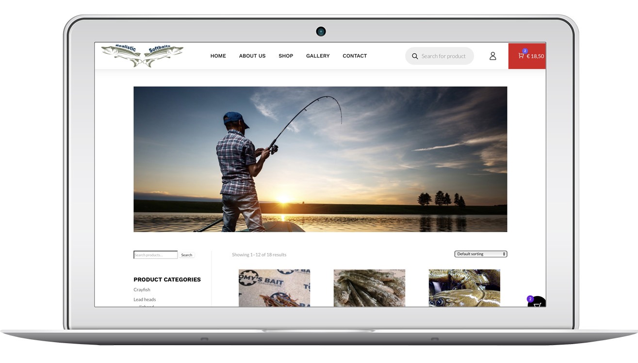 Strona internetowa sklepu 'realistic-softbaits.eu' na laptopie. W tle wędkarz łowiący ryby o zachodzie słońca. Kategorie produktów: Crayfish, Lead heads.