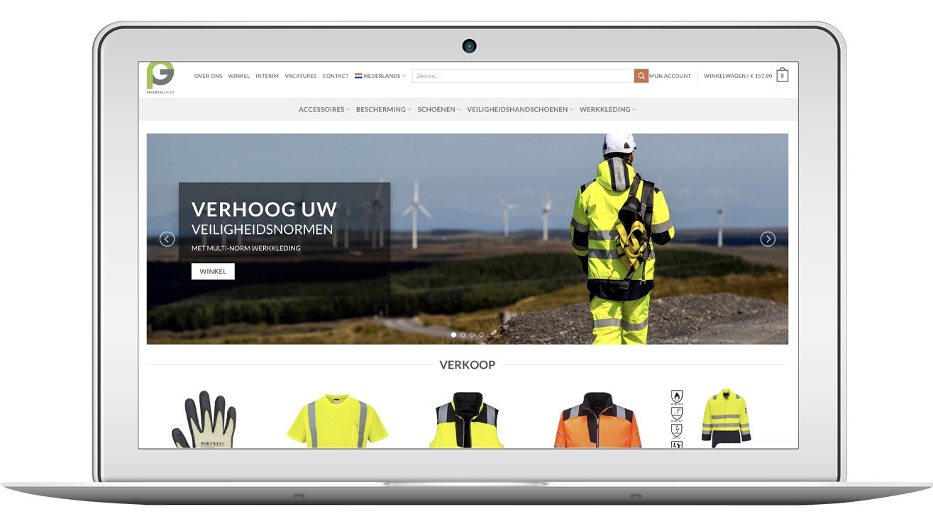 Laptop wyświetla stronę sklepu internetowego Progress Group z odzieżą roboczą. Widoczny slider z pracownikiem w odblaskowej kurtce na tle wiatraków i oferta rękawic, koszulek i kamizelek.