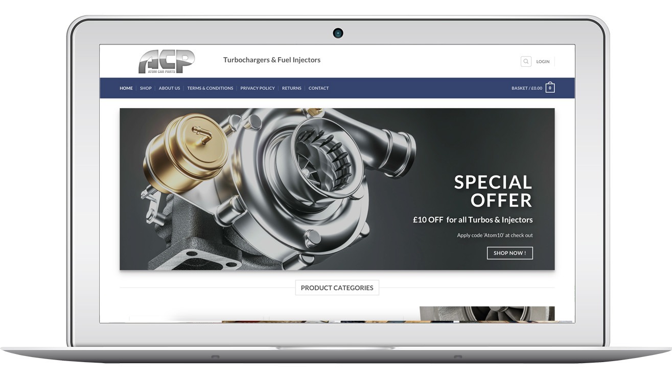 Laptop wyświetla stronę sklepu internetowego atomcarparts.co.uk z ofertą turbosprężarek i wtryskiwaczy. Widoczny baner z promocją i kategorie produktów.