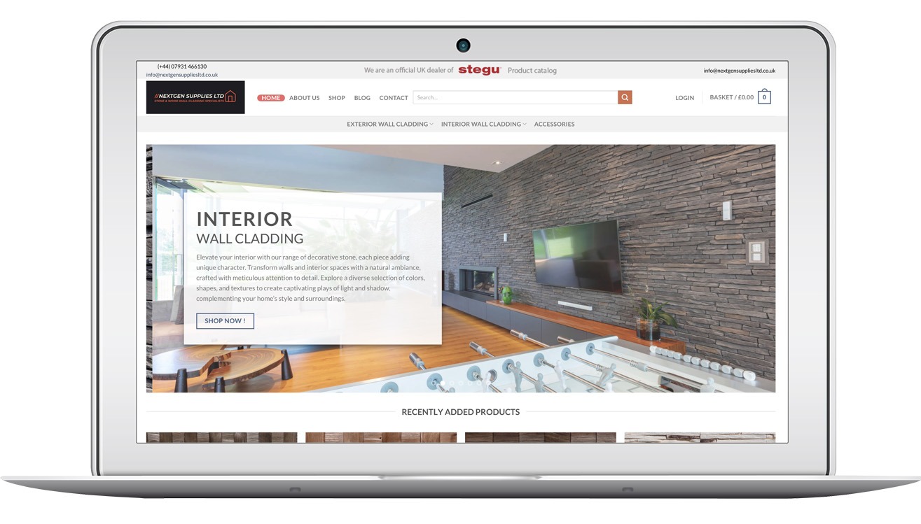Laptop wyświetla stronę nextgensuppliesltd.co.uk z ofertą okładzin ściennych. Widoczny fragment wnętrza z kamienną ścianą i telewizorem. Minimalistyczny design strony.