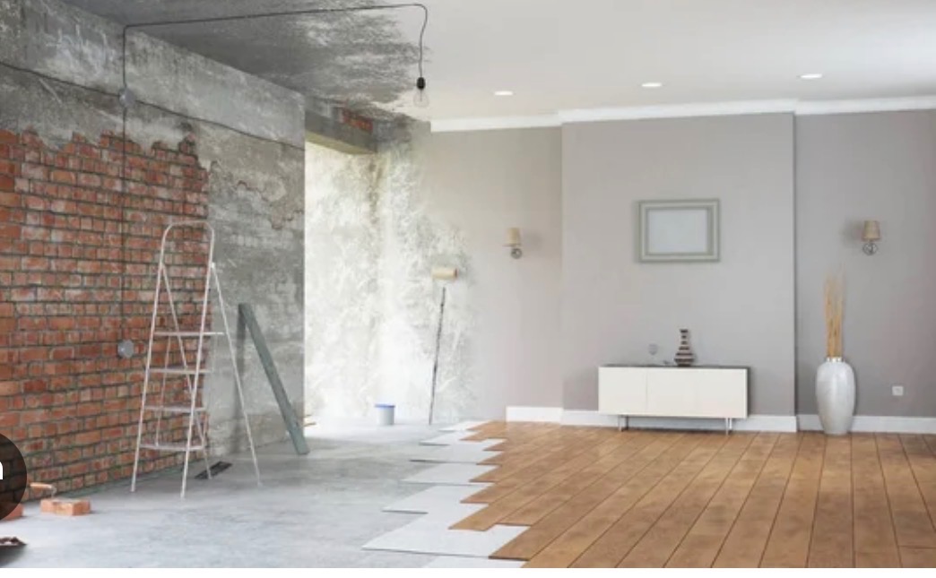 Wnętrze w trakcie remontu: surowa cegła, gładź, częściowo ułożona drewniana podłoga, drabina. Widoczne etapy prac wykończeniowych w pomieszczeniu.