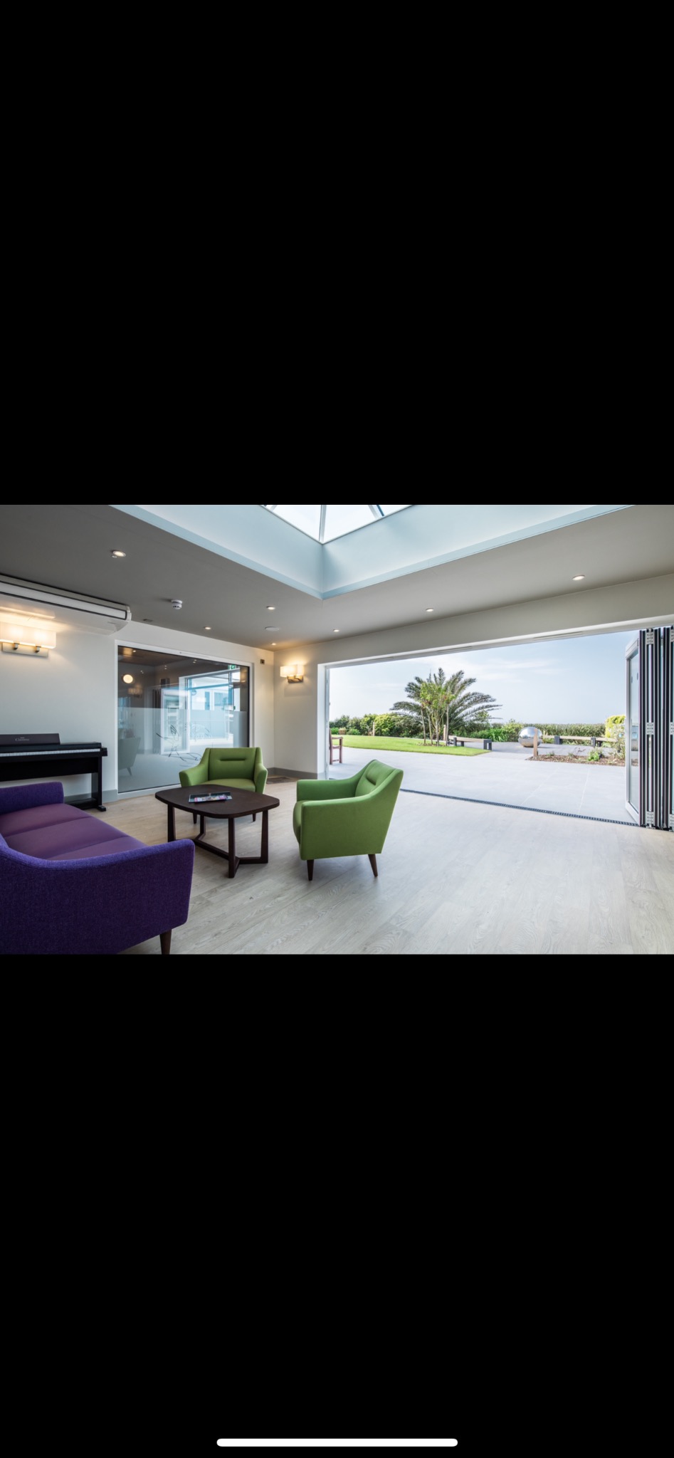 Jasne wnętrze z pianinem, zielonymi fotelami i fioletową sofą. Duże okno z widokiem na zewnątrz. Nowoczesny design z oknem dachowym i jasną podłogą.