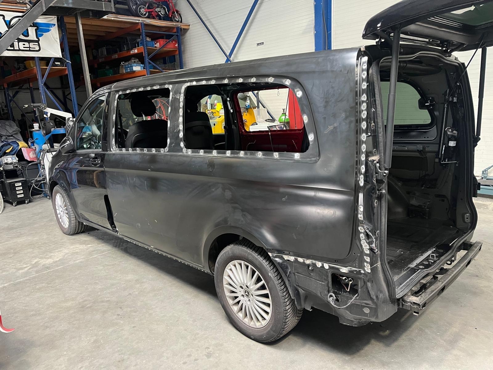 Czarny bus w trakcie prac blacharskich: wycięte okna, widoczne spawy. Karoseria przygotowana do lakierowania. Warsztat z wyposażeniem w tle.